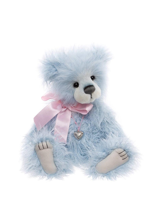 A light blue fluffy Charlie Bear sits upright against a white background, wearing a pink satin bow and silver heart locket necklace, with cream muzzle and paw pads.