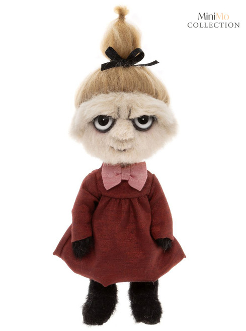 A small plush doll stands upright against a white background, wearing a dark red dress with a pink bow collar, black hands and feet, blonde upswept hair tied with a black ribbon, and a grumpy facial expression.