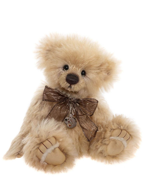 A fluffy cream-coloured Charlie Bears teddy bear sits upright, adorned with a shimmery bronze bow tie and a small decorative charm pendant, against a white background.
