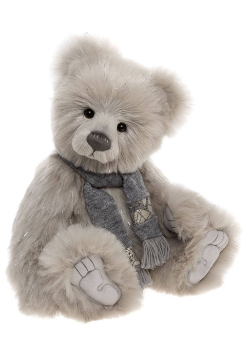 A soft grey plush teddy bear sits upright, wearing a grey knitted scarf with a decorative floral pattern and tassel ends, against a white background.