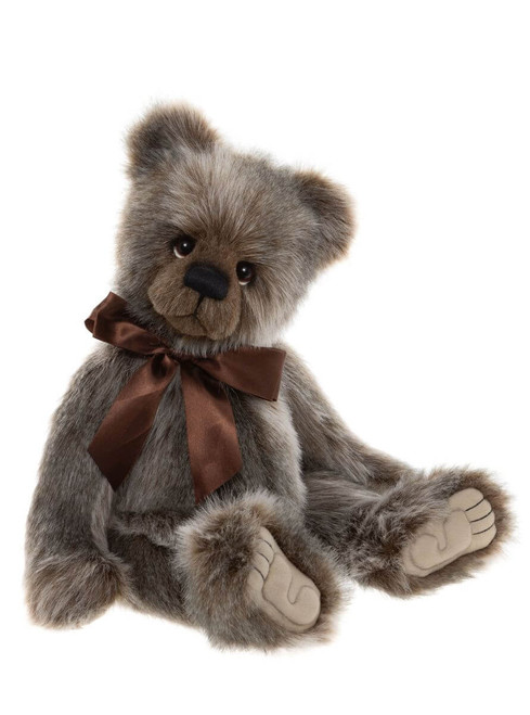 A grey-brown plush teddy bear sits upright against a white background, wearing a satin chocolate-brown bow tie. It has glass eyes, a black nose, and beige suede paw pads.