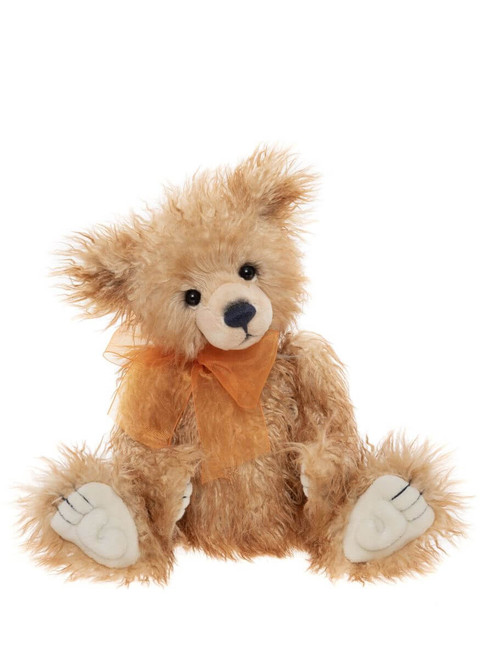 A fluffy golden-brown Charlie Bears teddy bear sits upright against a white background, wearing an orange organza ribbon bow at its neck, with white paw pads and tousled fur.