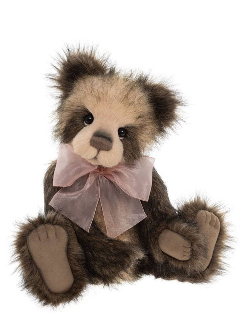 A dark brown plush Charlie Bears teddy bear sits upright against a white background, wearing a sheer pink ribbon bow around its neck, with suede-style paw pads visible.