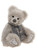 A soft grey plush teddy bear sits upright, wearing a grey knitted scarf with a decorative floral pattern and tassel ends, against a white background.