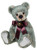 A grey-green plush teddy bear sits upright against a white background, wearing a dark burgundy satin bow tie adorned with a small gold jingle bell.