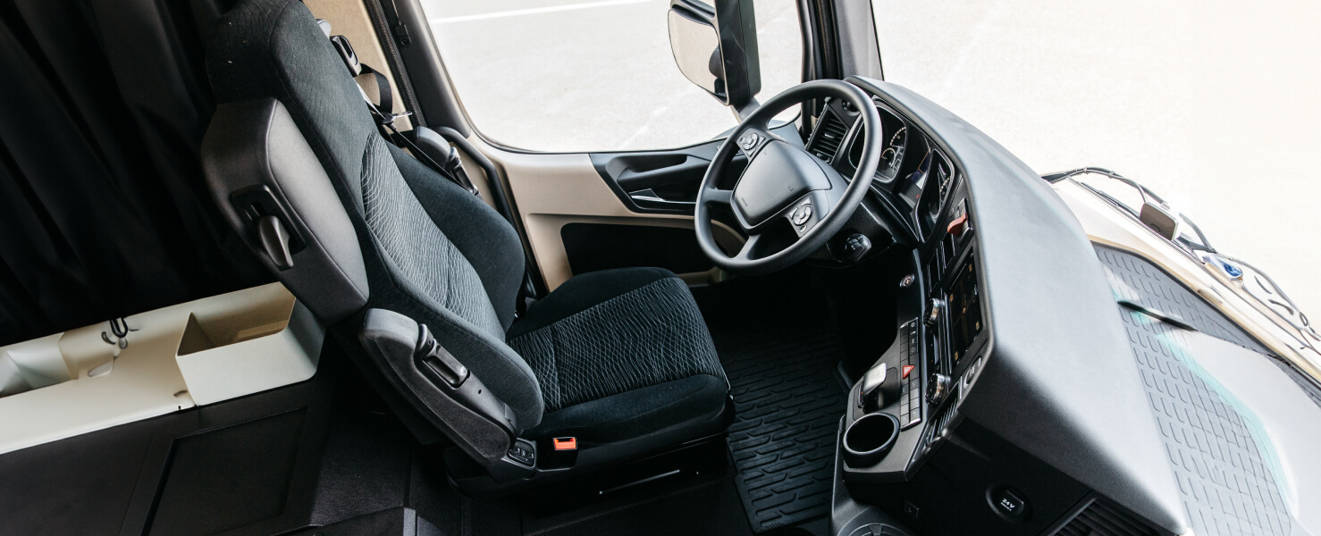 Truck cab interior with driver seat, steering wheel, and dashboard controls.