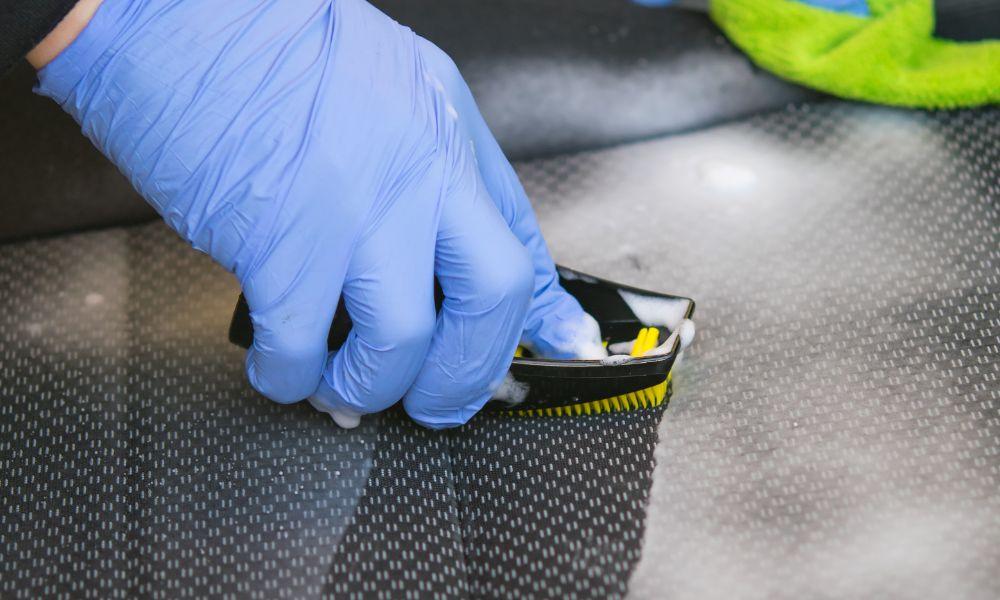Gloved hand scrubbing a dark leather truck seat with a cleaning brush, demonstrating proper technique for maintaining aftermarket leather truck seats and extending their lifespan