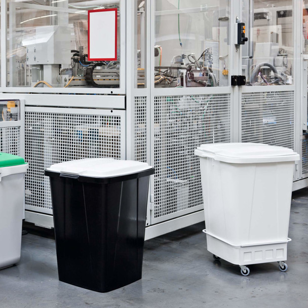 White Durabin 90 Installed in a Dolly & Fitted with a White Lid, Situated Next to Black Durabin 90 Fitted with White Lid & Positioned Alongside Machinery