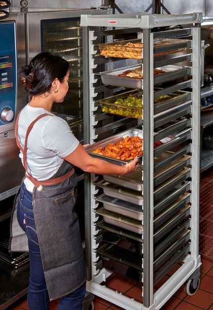 UGNPR11F18480 - Kitchen worker standing by commercial ovens inserting 65mm stainless steel pan containing chicken wings into trolley