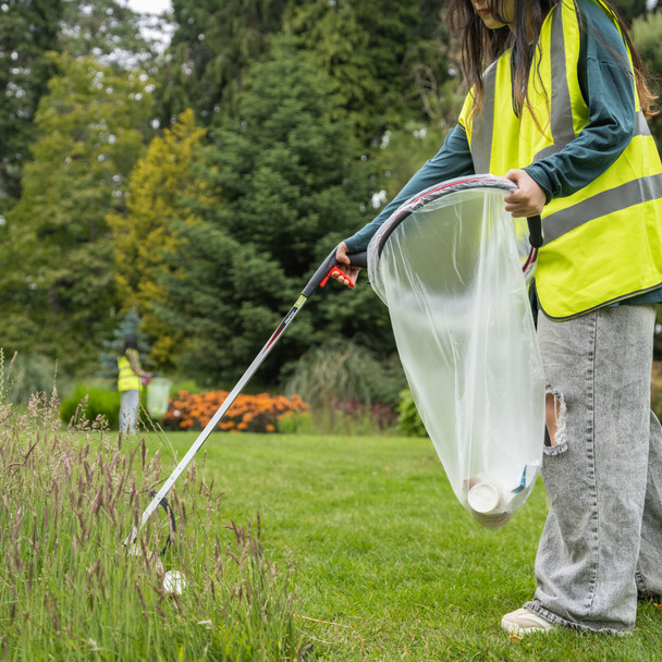 Female in Hi-Vis Vest Collecting Litter from Long Grass Using the Community Litter Picker with a Handi-Hoop in Their Other Hand