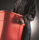 FG352600RED - A person carrying the red Rubbermaid Square Brute using the moulded handles