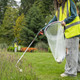 Female in Hi-Vis Vest Collecting Litter from Long Grass Using the Community Litter Picker with a Handi-Hoop in Their Other Hand