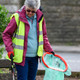 A lady wearing a hi-vis vest holds the handi-hoop fitted with green liner in one hand and a litter picker in the other