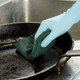 A person wearing blue gloves cleaning a heavily burnt frying pan using a Mercury 96 Small Green Scouring Pad