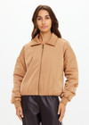 THE UPSIDE women's tan Carlotta Bomber Jacket is made from recycled fabric and made for a cropped fit. This fully insulated jacket features side seam pockets and metal arrow logo zipper.