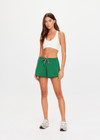 THE UPSIDE women's green recycled Austen Run Short made from quick drying performance fabric features a curved hem with cotton lace scalloped edge detailing, navy in-built shorts and invisible zip pockets. Made for running, tennis, golf & pickleball.