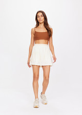 THE UPSIDE women's creme pleated Mansi Amy Skirt made in Recycled Polyester lightweight mesh fabrication features a stripe waistband, inner stretch short with pockets, printed arrow logo and moisture wicking properties.
