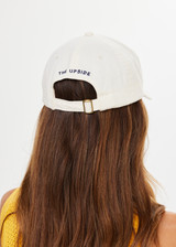 THE UPSIDE women’s cream Good Luck Soft Cap features an embroided 'Good Luck' on front with an adjustable strap at the back.