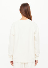 THE UPSIDE women’s creme cotton Hamsa Sunday Long Sleeve features a relaxed fit, dropped shoulders, and an embroidered evil eye on the sleeve. Perfect for layering.