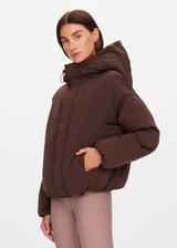 THE UPSIDE women's brown Mercer Hooded Puffer Jacket is fully lined and features invisible zip pockets with fleece lining, soft elasticated cuffs, a hood and is made from recycled fabric. Made for lifestyle.