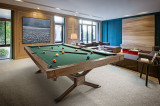 Brunswick Billiards Brunswick 8' Dameron Slate Pool Table, a wooden billiard table with green felt surface and pool balls set up, located in a modern living room with large windows, a TV, and cozy seating.