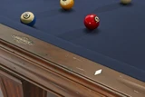 Brunswick Billiards Brunswick Glenwood Slate Pool Table in Tuscana, showing a close-up of the blue felt surface with billiard balls and the wooden edge with a Brunswick logo.
