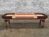 Venture Shuffleboard Grand Deluxe Bank Shot 9' Shuffleboard Table, made in USA, featuring a polished wooden surface with red accents, sturdy legs, and built-in scoring system.