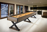Brunswick Billiards Brunswick Premier Shuffleboard Table, modern indoor game room with large windows, black and wood finishes, and sleek decor.