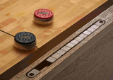 Brunswick Billiards Brunswick Botanic Shuffleboard Table | Rustic Dark Brown & Charcoal, close-up of the shuffleboard playing surface with pucks in red and black, and the edge with triangular scoring areas.