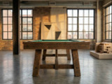C.L. Bailey Tunbridge Pool Table in Weathered Brown, showcasing a rustic wooden design in an industrial-style room with large windows and exposed brick walls.