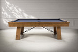 Side profile photo shoot view of the Plank & Hide Isaac slate pool table in Glazed Maple, featuring maple wood construction, Championship Academy Blue felt, black pockets, and industrial metal support details.