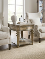 Hooker Furniture Castella End Table, rustic wooden side table with a distressed finish, single drawer with decorative knob, lower shelf with decorative bowl, in a stylish living room with elegant armchairs and accessories.