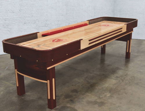 Venture Shuffleboard Grand Deluxe Bank Shot 9' Shuffleboard Table, made in USA, featuring a wooden playing surface with scoring zones and a red puck, set on a sturdy wooden frame with a corner bumper for gameplay.