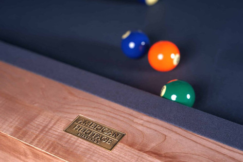 American Heritage Billiards American Heritage Finish Samples, close-up of the wooden billiards table edge with a metal plaque and pool balls in the background.