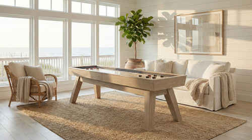 Doc & Holliday George 12ft Shuffleboard Table – Natural Ash, stylish indoor shuffleboard table in a bright living room with large windows, a white sofa, and plants.