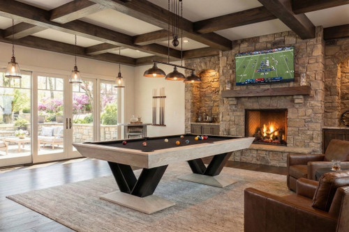 Doc & Holliday Savant 8' Slate Pool Table in Natural Ash, in a cozy living room with a stone fireplace, ceiling beams, and large windows.
