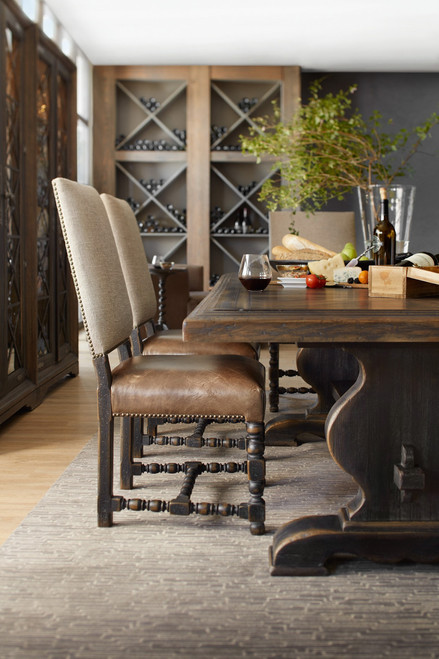 Hooker Furniture Bandera 86-inch Table with 2-18-inch Leaves, wooden dining table set in a modern dining room with beige upholstered chairs, wine and food on the table, and a wine rack in the background.