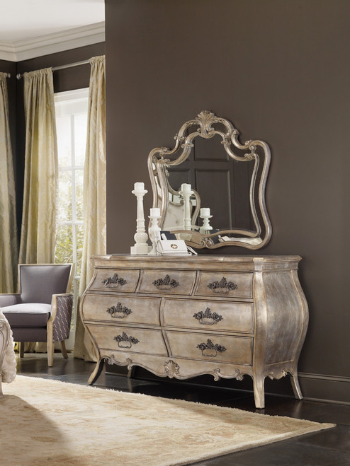 Hooker Furniture Sanctuary Dresser, vintage-style antique silver dresser with ornate details and curved lines, topped with a decorative mirror and white candlesticks in a luxurious bedroom setting.