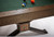 Brunswick Billiards Brunswick 8' Dameron Slate Pool Table, close-up of the wooden rail and pedestal base with Brunswick logo, featuring a green felt playing surface and billiard balls.