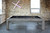 Brunswick Billiards Brunswick Sanibel Slate Pool Table in Rustic Grey, showing a pool table in rustic grey wood with black felt surface, set against an exposed brick wall with a neon cross artwork, in a modern game room.