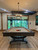 Brunswick Billiards Brunswick Birmingham Slate Pool Table, Charcoal, in a modern game room with wooden floors and large windows showing a wooded outdoor scenery.