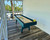 Venture Shuffleboard Mason Sport Shuffleboard Table by Venture, in a bright indoor space with large windows and a view of palm trees outside.