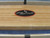Playcraft Telluride Honey Shuffleboard Table with optional Overhead Electronic Scoring, showing the wooden playing surface and the Playcraft logo in the center.