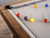 Plank & Hide Co Isaac Slate Pool Table by Plank & Hide, distressed brown and gold finish. Showcasing a close-up view of the table's wooden edge and pool balls on the slate surface.