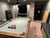 Plank & Hide Co Beaumont Pool Table by Plank & Hide in distressed brown finish, set in a game room with brick walls and a classic arcade game in the background, featuring free installation.