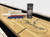 Playcraft Georgetown Espresso Shuffleboard Table, close-up view of the wooden shuffleboard surface with scoring area and shuffle pucks and wax.