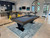 Doc & Holliday Savant 8' Slate Pool Table in Brown Sugar Finish, modern pool table with black legs, placed on a patterned rug in a stylish room with seating, artwork, and decorative window.