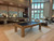 Doc & Holliday Paula Parsons Slate Pool Table, a stylish pool table with a black surface and wooden frame, set in a modern lounge with high ceilings and large windows.