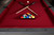 Doc & Holliday Hepburn Slate Pool Table, featuring a red felt surface with pool balls arranged in a triangle, and two crossed cues on top.