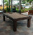 Sawyer Twain Metro All Weather Outdoor Pool Table with Storage Drawer, featuring a modern design with a beige felt surface, situated in an outdoor patio area with lush greenery and poolside seating.